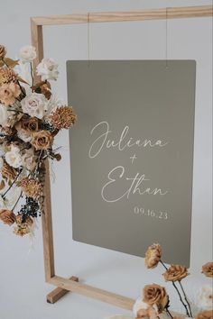 a sign with flowers hanging from it next to a wooden frame and some dried flowers