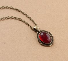 This beautiful Victorian style necklace is made from antique bronze chain and dark red cabochon housed in an ornate filigree setting. -the chain is 18 inches length -the pendant is approximately 1 inch long and 0.75 inch wide including the setting -lobster claw closure SHIPPING: Default shipping is by regular mail, which does not have tracking, shipping times are as follows: US: 1-2 weeks Canada: 1-2 weeks Europe: 2-3 weeks If you would like to add tracking for your parcel, please upgrade to Exp Red Gothic Necklace, Red Jewel Necklace, Antique Red Oval Pendant Jewelry, Antique Red Brass Necklace, Red Vintage Necklace With Cabochon, Vintage Red Oval Pendant Necklace, Vintage Red Cabochon Necklace, Red Oval Pendant Vintage Necklace, Red Vintage Oval Pendant Necklace