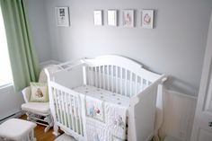 a white crib in a baby's room with green drapes and pictures on the wall