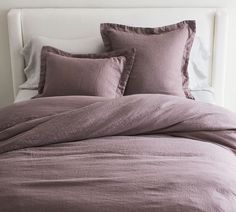 an unmade bed with purple linens and pillows on it's headboard