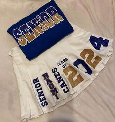 two white and blue cheerleader skirts with gold letters on them sitting on a bed