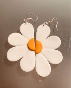 a pair of white and orange flower shaped earrings on a gray surface with silver earwires