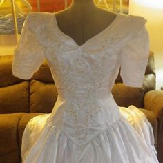 a white wedding dress sitting on top of a table next to a brown couch in a living room