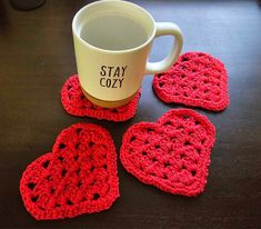 four crocheted coasters sitting on top of a table next to a coffee cup