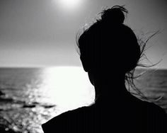 a woman standing in front of the ocean with her hair blowing in the wind at sunset