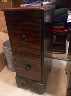 a wooden cabinet sitting on top of a floor next to a trash can and chair