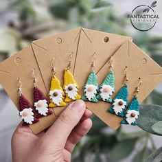 a person holding up some earrings in front of a flowered plant and brown card