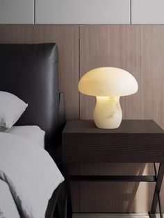 a white mushroom lamp sitting on top of a night stand next to a black bed