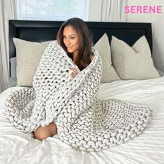 a woman laying on top of a bed covered in a knitted blanket and smiling