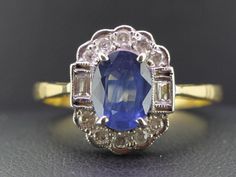 "The simplicity of this ring adds a wonderful statement of elegance. This gorgeous ring would be the perfect Sapphire anniversary ring or 'something blue' for a Vintage bride. Boosting an oval 1.40 carat rich royal blue Ceylon Sapphire secured in a classic four prong setting. Taking center stage amongst half a carat of bright white high premium sparkling Diamonds. The Ceylon Sapphire is flanked by two mille grained set sparkling baguette Diamonds boarded by ten brilliant cut claw set collet edge Classic Blue Halo Ring, Classic Blue Halo Ring For Formal Occasions, Classic Oval Sapphire Wedding Ring, Classic Sapphire Cluster Ring For Wedding, Elegant Blue Oval Cluster Ring, Vintage Blue Oval Cluster Ring, Sapphire Anniversary Ring, Sapphire Anniversary, Gorgeous Ring