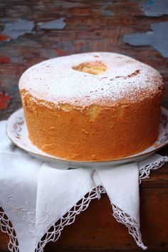 a cake sitting on top of a white plate covered in powdered sugar next to a wooden table