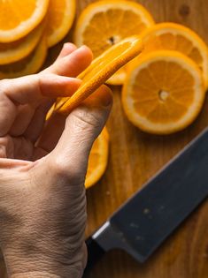 a person holding an orange peel in front of sliced oranges