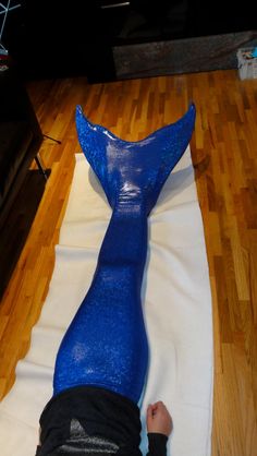 a person laying on top of a wooden floor next to a blue plastic mermaid tail