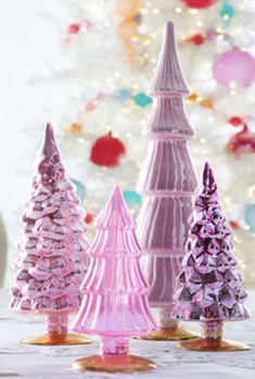 pink and purple christmas trees sitting on top of a table next to a white christmas tree