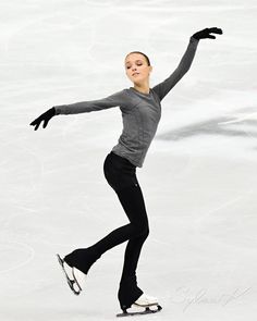 a woman skating on an ice rink in a gray shirt and black pants with her arms outstretched