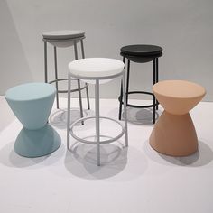 four stools in different colors and sizes on a white surface with no one around them