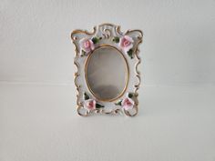 a mirror with pink flowers on it sitting on a table next to a white wall