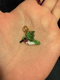 a person's hand holding a small green and white beaded keychain