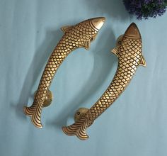 two gold fish shaped door handles on a blue surface with purple flowers in the background