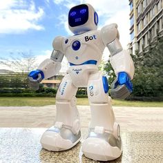 a white robot standing on top of a table next to a tall building and blue sky