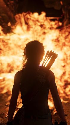 a woman standing in front of a fire with her back to the camera and holding two arrows