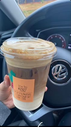 a person holding up a cup of coffee in their hand and steering wheel behind them