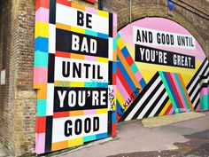 a woman is walking down the street in front of some colorful wall art and there's a car parked next to it