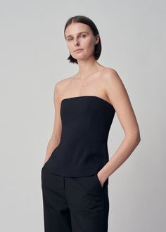 Strapless bustier top with interior boning detail, slim silhouette, and hip length for easy tucking. Details Strapless black bustier top Fitted silhouette Flexible boning Invisible back zip 97% Viscose 3% Elastane 1178MBND-ESSN Fits true to size. Take your normal size. Model is 5'10" and wears a size Small. Black Tops With Built-in Bra And Fitted Bodice, Chic Tops With Built-in Bra And Fitted Bodice, Sleeveless Evening Tops With Built-in Bra, Elegant Structured Tops For Night Out, Sleek Strapless Top For Night Out, Black Fitted Bodice Tube Top, Elegant Top With Minimal Stretch For Night Out, Black Fitted Boned Bodice Top, Elegant Top For Night Out With Minimal Stretch