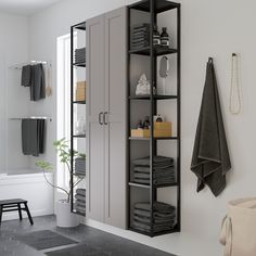 a white bathroom with black shelving and towels on the shelves, along with a potted plant