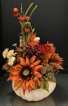 a white pumpkin filled with lots of different types of flowers and leaves on top of a table