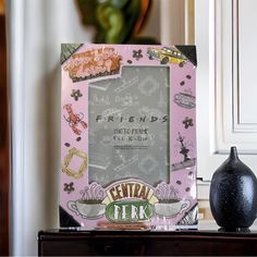 a black vase sitting on top of a table next to a pink frame with pictures