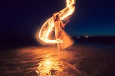 a woman is standing on the beach with fire in her hand and holding a surfboard