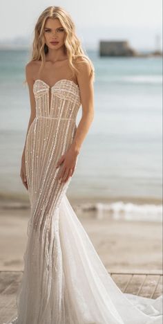 a woman in a white dress standing on a pier next to the ocean and looking at the camera