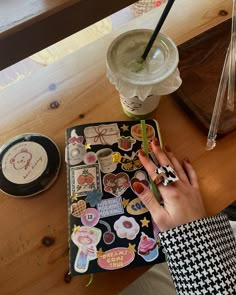 a person's hand on top of a notebook covered in stickers next to a cup of coffee