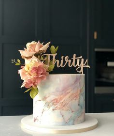 a marble cake with pink flowers and the word thirty on top is sitting on a table