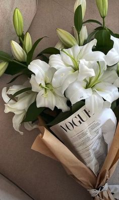 a bouquet of white flowers sitting on top of a couch next to a paper bag