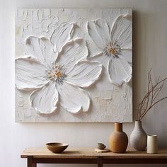 a white flower painting on a wall above a wooden table with vases and bowls