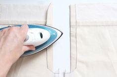 a person ironing fabric with an electric iron on a white table cloth, while someone is using a blue and white iron