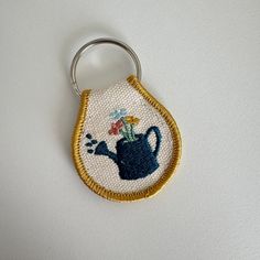 an embroidered keychain with a teapot and flowers on it's side