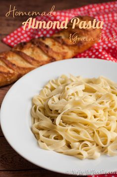 a white plate topped with pasta on top of a wooden table next to some bread