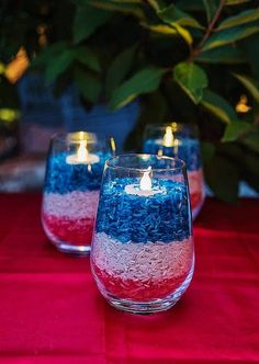 three candles that are sitting in some glass vases with red, white and blue decorations