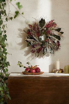 a wreath is hanging on the wall above a table with apples and other decorations in front of it