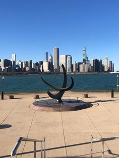 a large metal sculpture in front of a body of water with a cityscape in the background