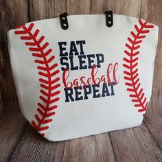 an embroidered baseball bag with the words eat sleep baseball repeat written on it, sitting on a wooden surface