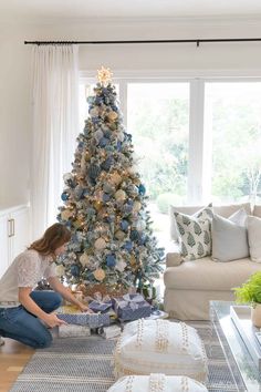 a woman sitting on the floor in front of a christmas tree with presents under it