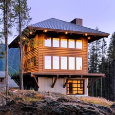 a large wooden house sitting on top of a hill next to trees with lights on the windows