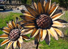 two metal sunflowers sitting on top of a grass covered field next to each other