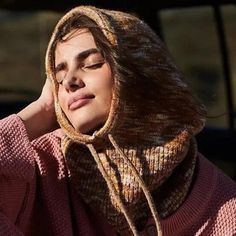 a woman wearing a pink sweater with a hoodie over her head and looking off to the side