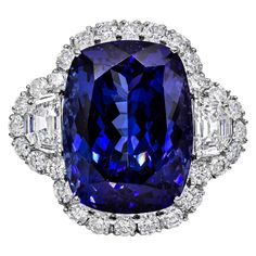 A well-crafted high-end cocktail ring, showcasing a large 26.35 carats cushion cut tanzanite, set on a classic four prong setting. Surrounded by a halo of round brilliant cut diamonds and flanked by two epaulette cut diamonds. Accented with a diamond encrusted shank on a half-way design. Accent diamonds weigh 4.52 carats total. Set elegantly on an 18K white gold mounting. Size 7 US, resizable upon request. Roman Malakov is a custom house, specializing in creating anything you can imagine. If you Sapphire Cocktail Ring, Diamond Rings With Price, Contemporary Engagement Rings, Tanzanite Diamond Ring, Sapphire Rings, Jewels Rings, Three Stone Diamond, Diamond Jewelry Designs, Diamond Cocktail Rings