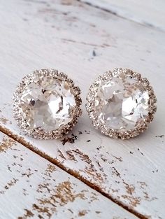 two pairs of earrings sitting on top of a wooden table with white paint and glitter